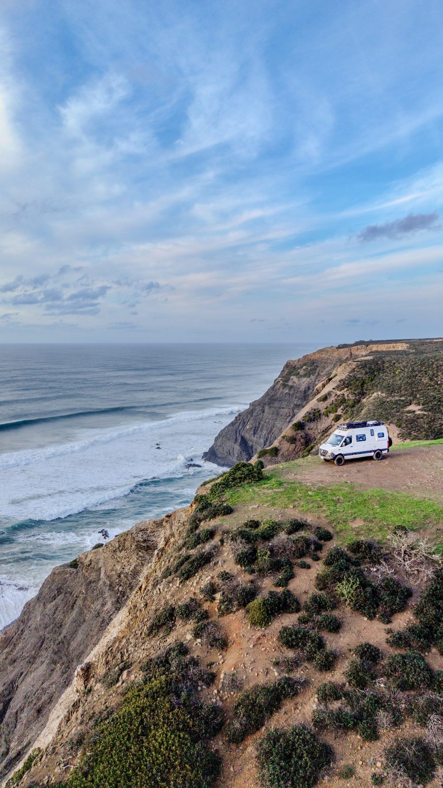 Aerial view of a Mercedes Sprinter 4x4 camper parked on a grassy clifftop above the sea