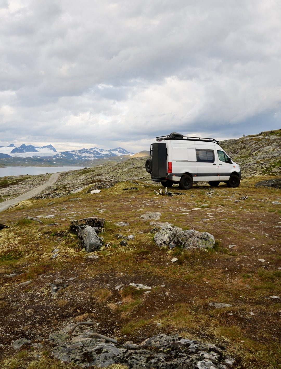 Mercedes Sprinter 4x4 camper parked on open highland with distant snowy mountains and a lake