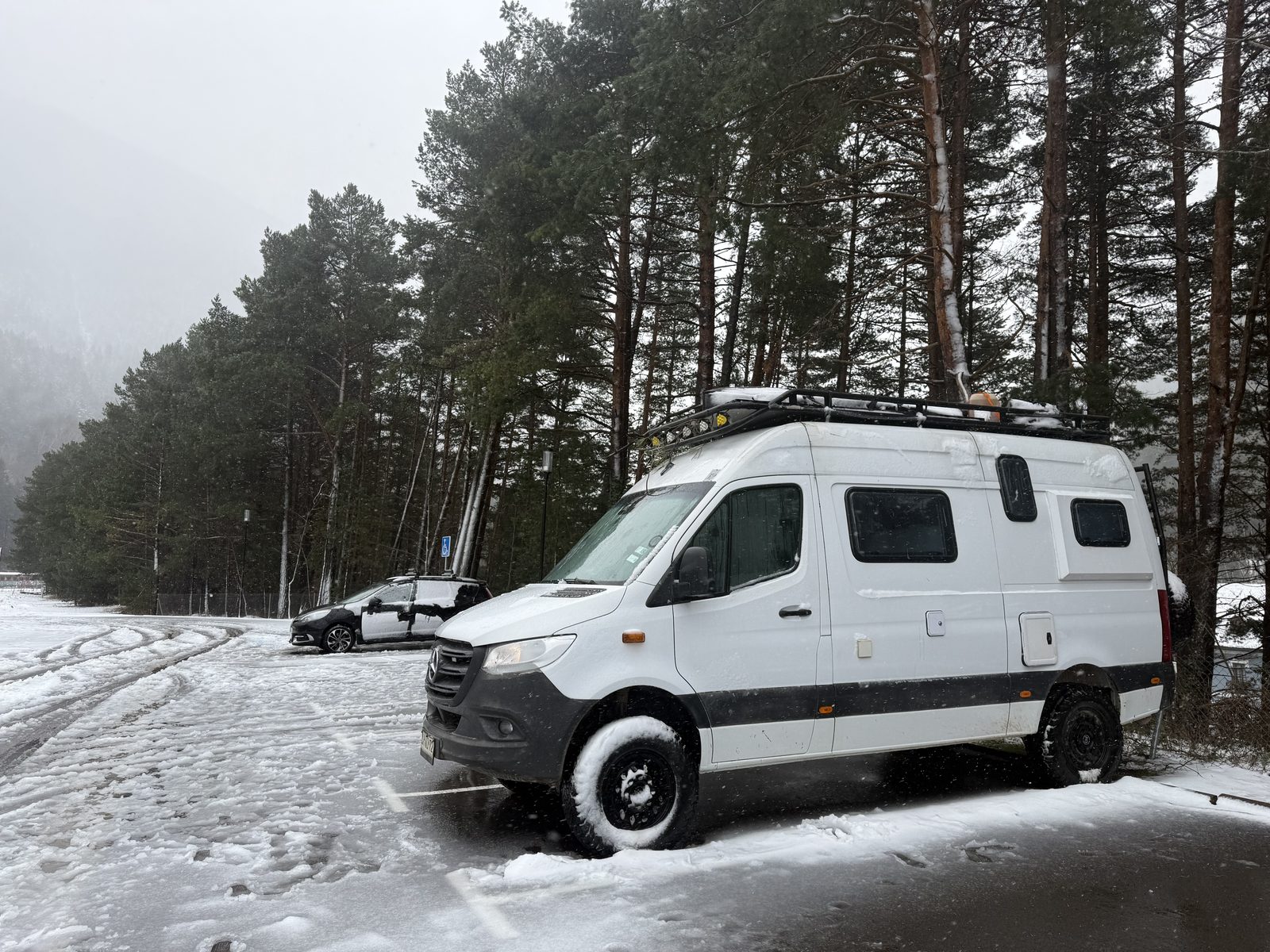 Mercedes Sprinter 4x4 camper parked among pine trees on a snowy road