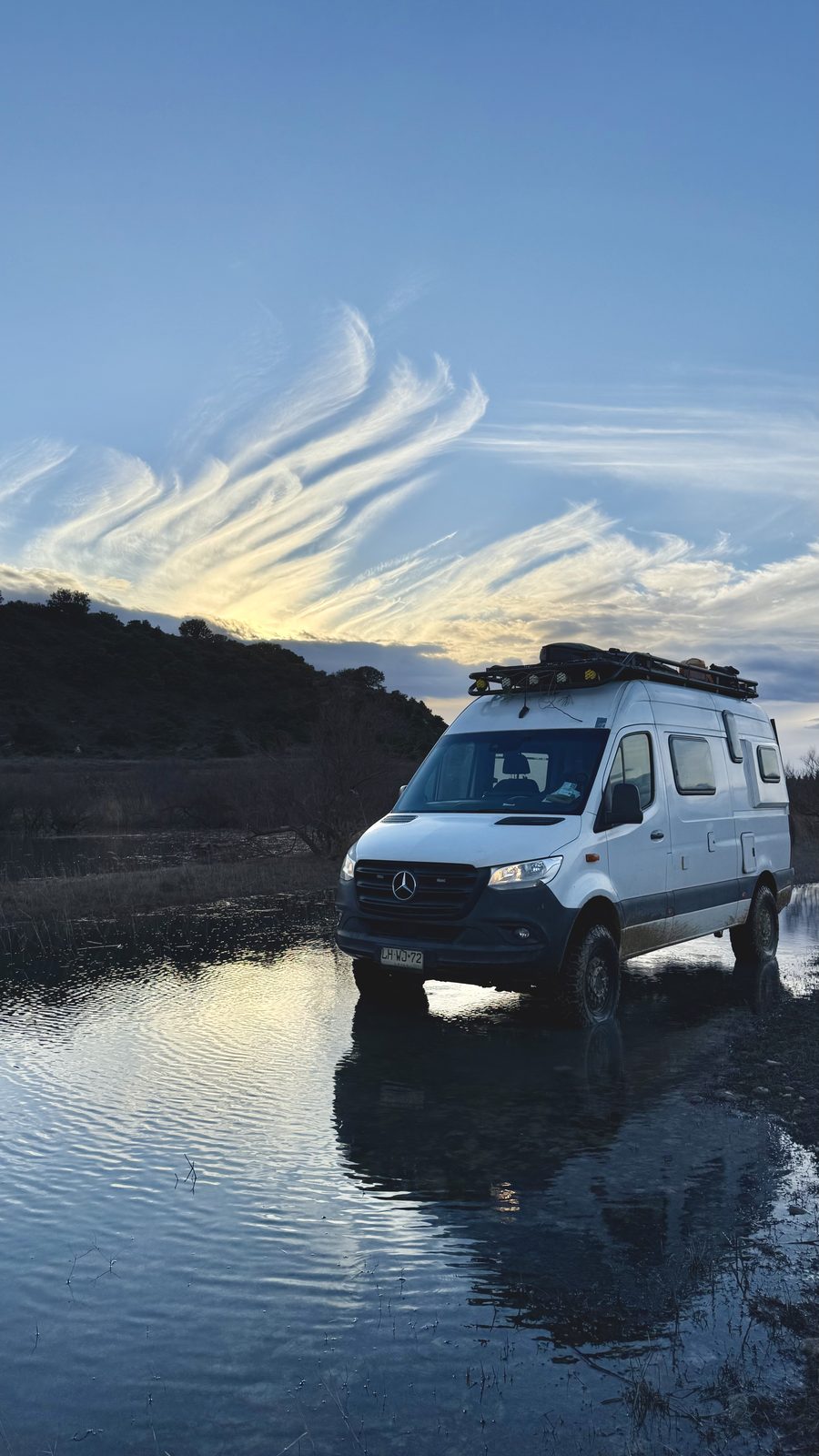 Mercedes Sprinter 4x4 camper reflected in still water at sunset