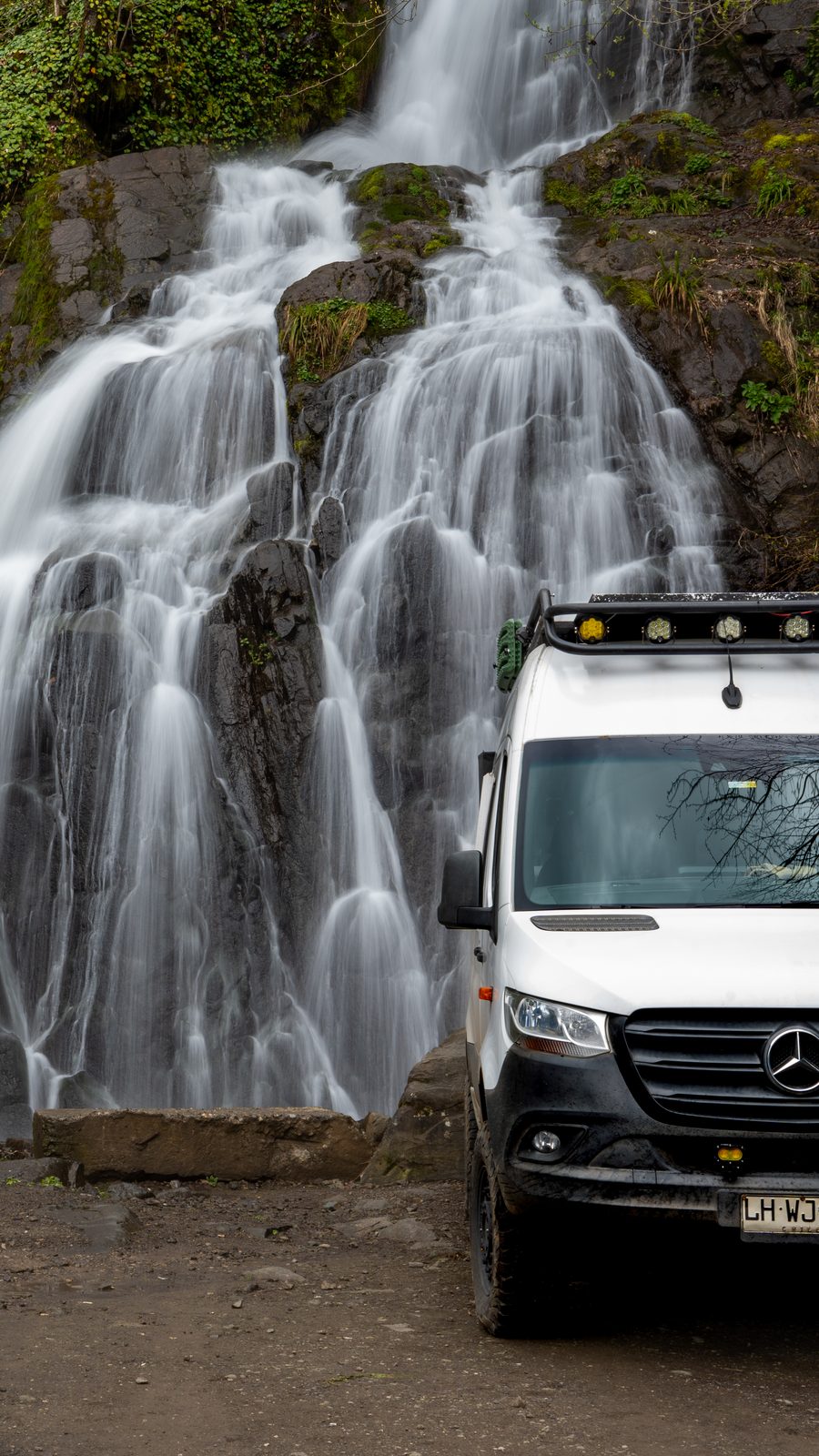 Mercedes Sprinter 4x4 camper parked in front of a tall waterfall