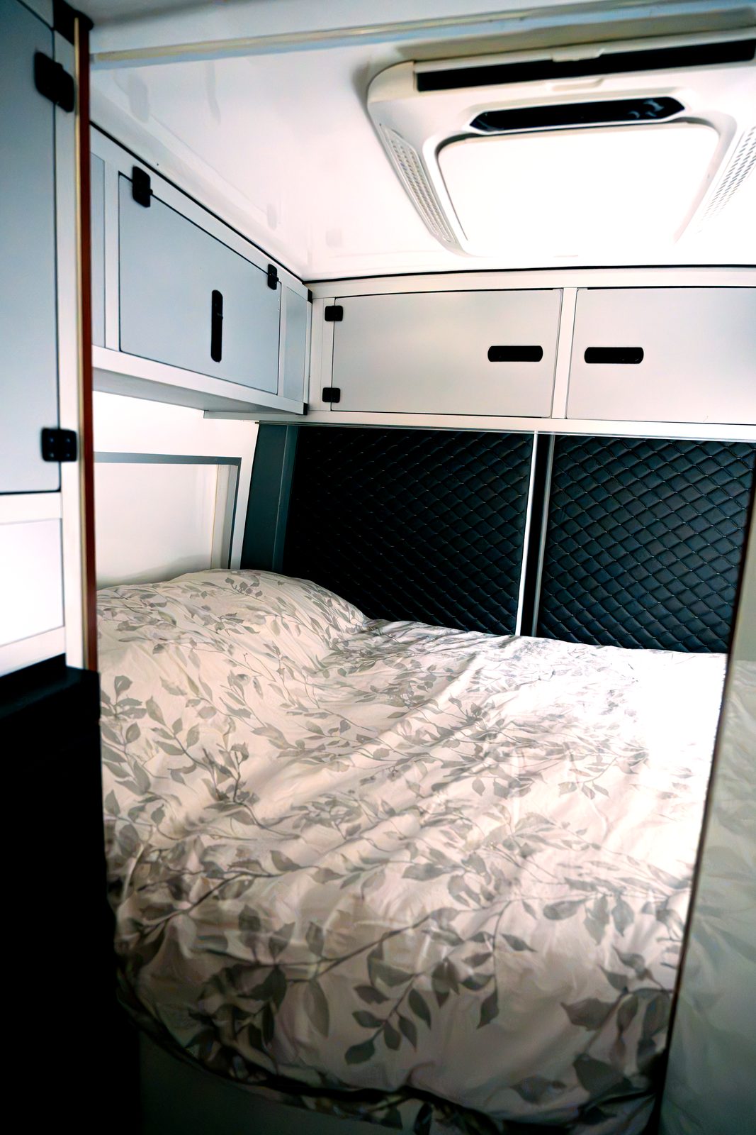 Queen-size bed inside the Mercedes Sprinter 4x4 camper with floral bedding and overhead cabinets