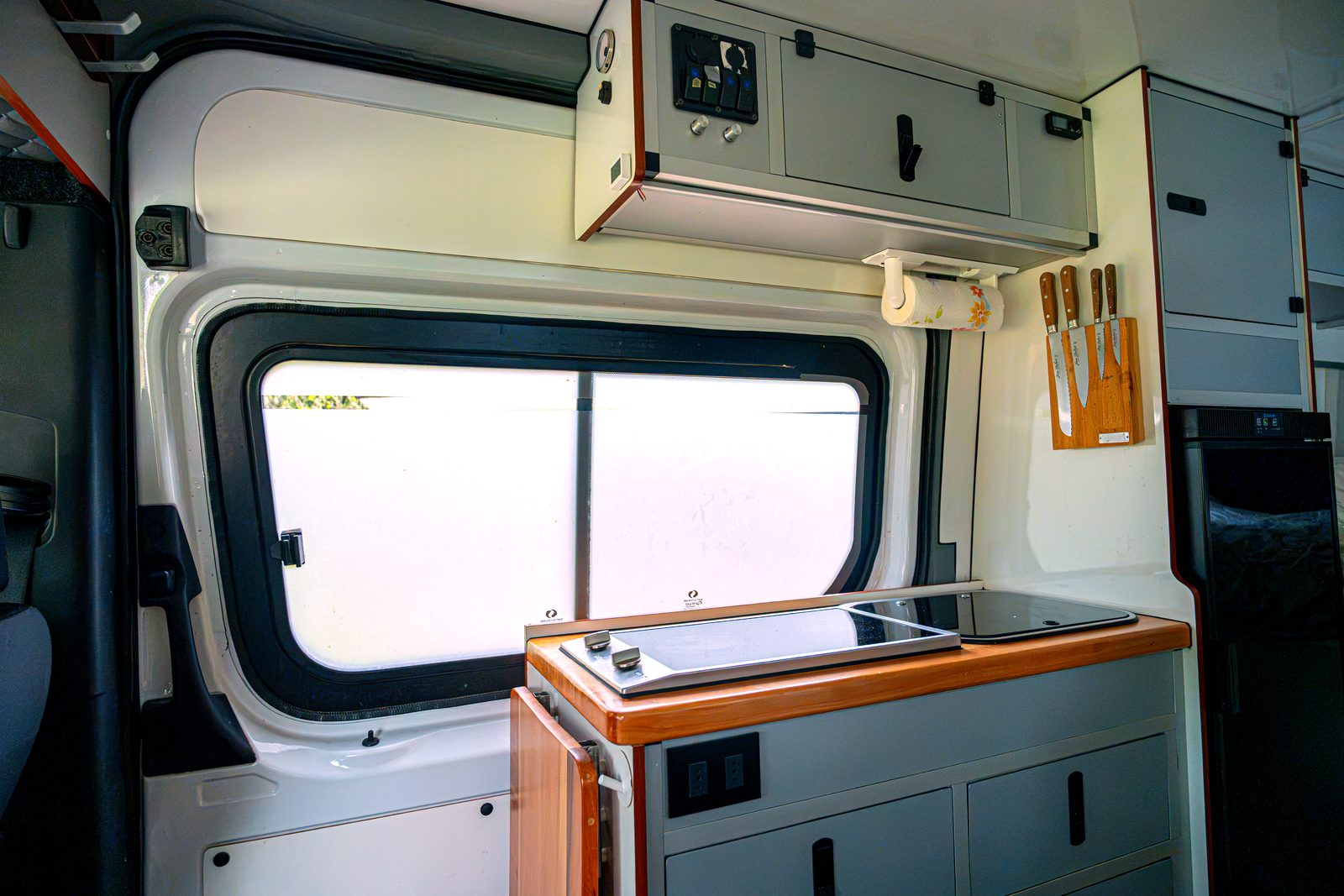 Camper kitchen in daylight with induction cooktop, knives and cabinets